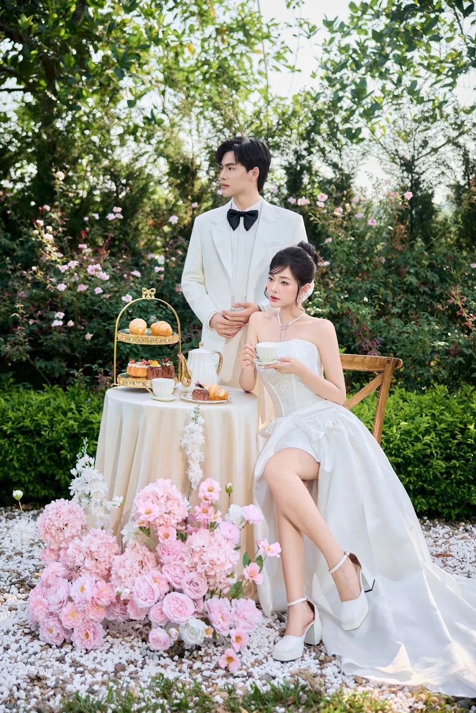 Cặp đôi bên bàn trà giữa vườn, phía trước là hoa hồng phấn